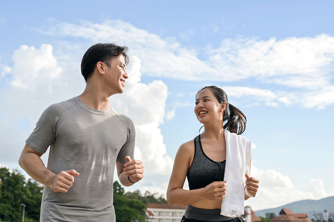 Asian couple wearing sportswear smiling and running together, enjoying outdoor exercise and a healthy lifestyle.
